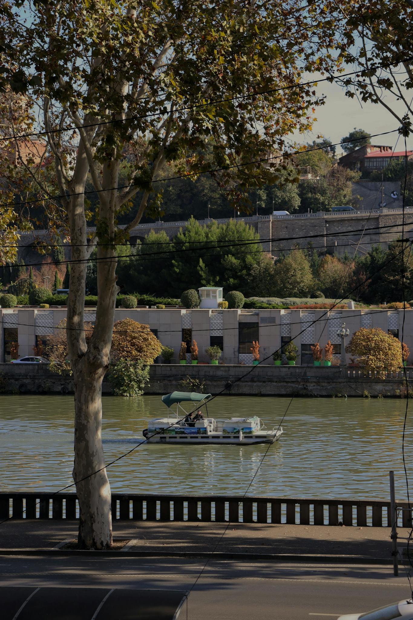 A picturesque scene of the river in Tbilisi, Georgia, featuring a motorboat and lush greenery.