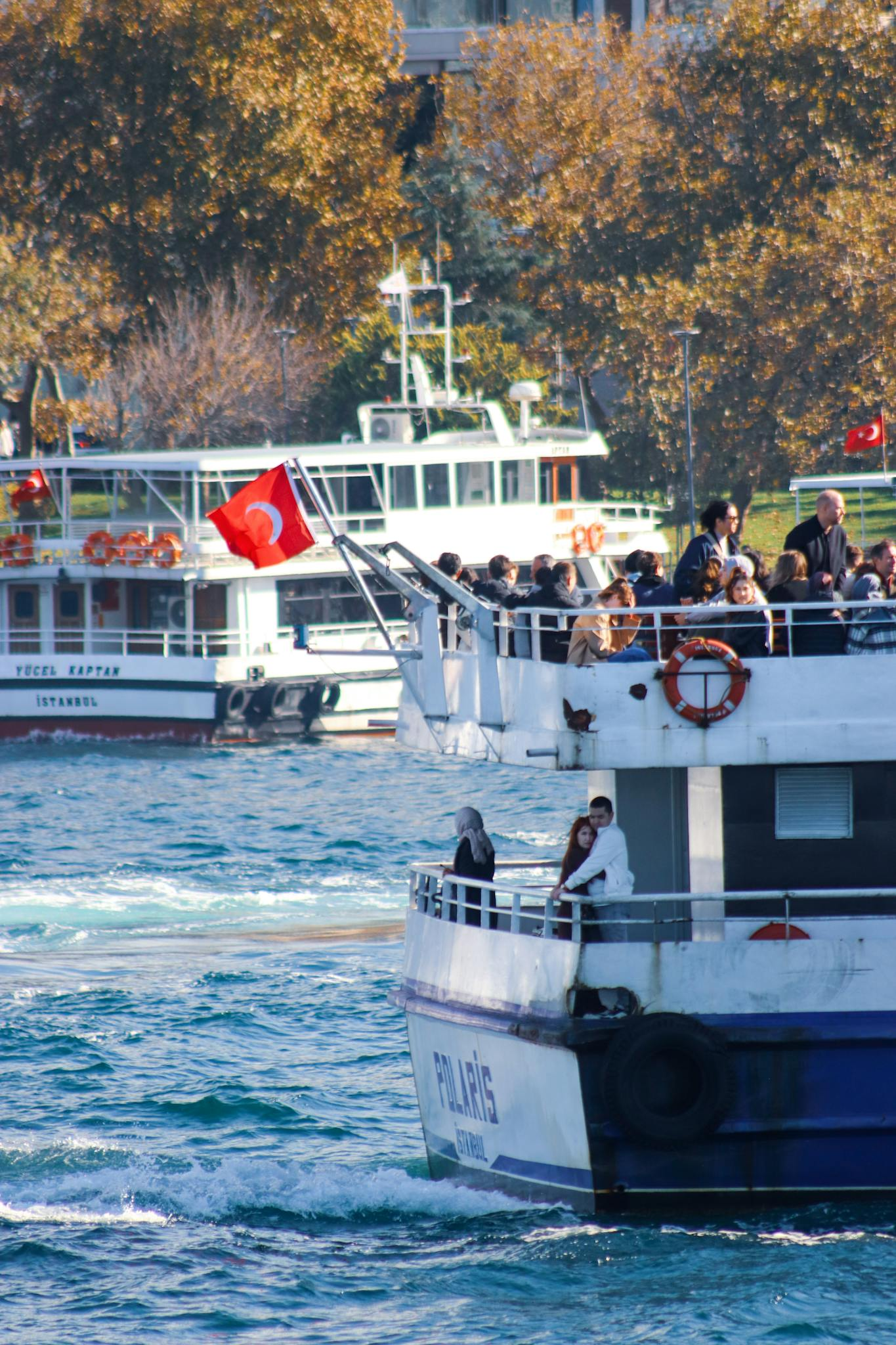 Ferry carrying passengers on the Bosphorus in Istanbul with Turkish flags waving.